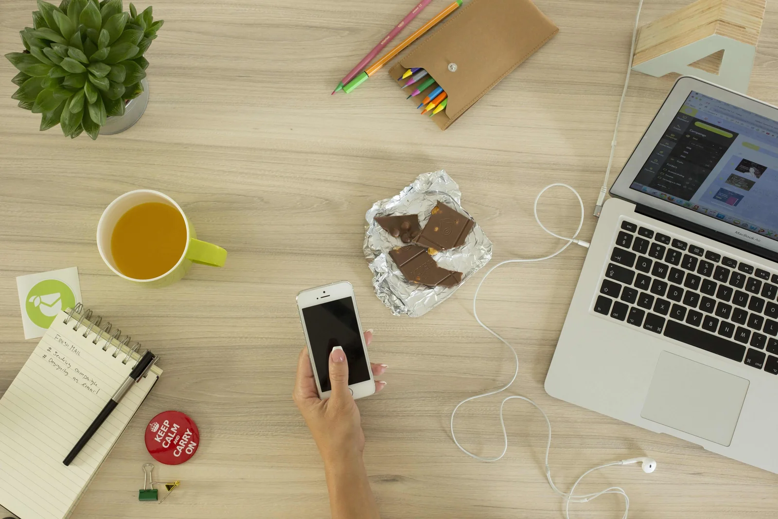 Hand holding a smartphone next to a laptop on a light wooden desk, the everyday setup for a Backpack Wallet review