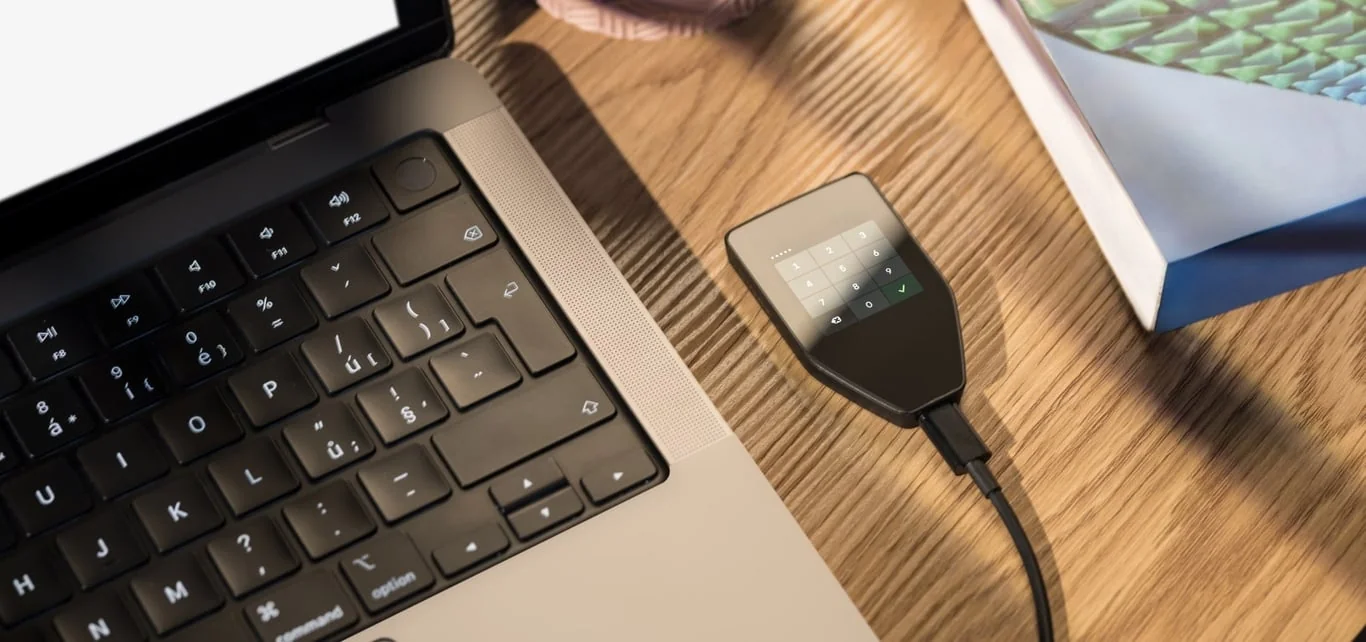Trezor Safe 5 hardware wallet beside a laptop, showing the PIN keypad on its color touchscreen