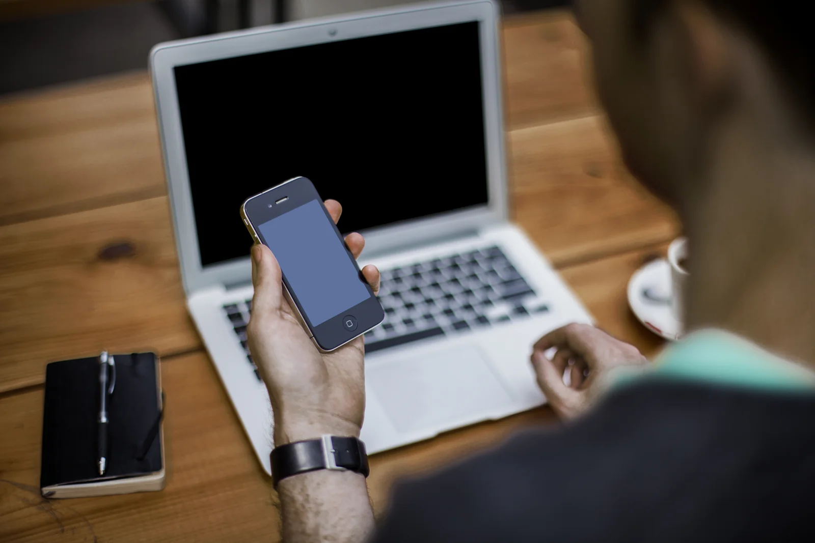 Person holding a smartphone in front of a laptop, the two devices beginners use to set up their first crypto wallet