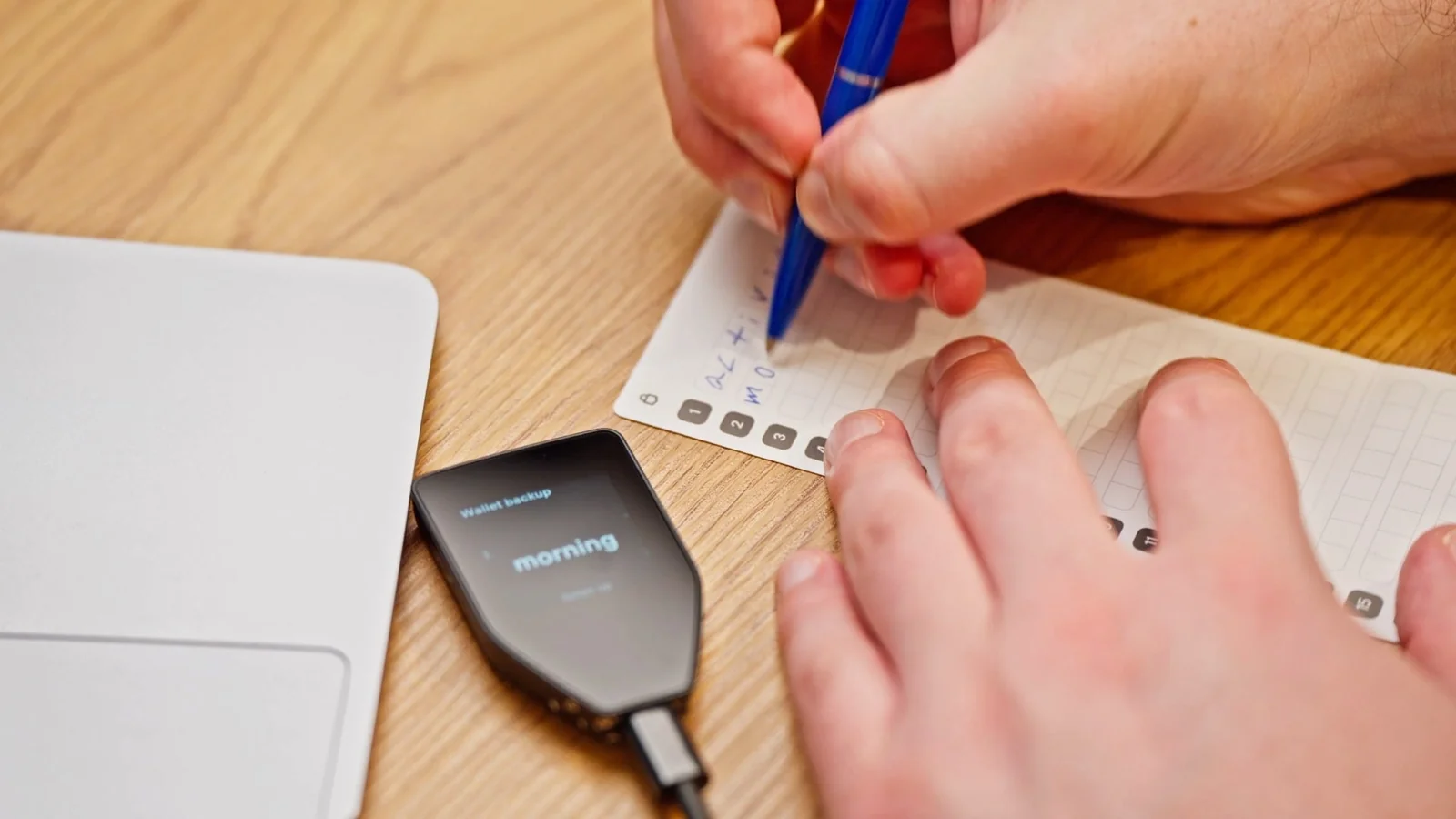 Trezor Safe 5 hardware wallet on a desk while a user writes down the wallet backup