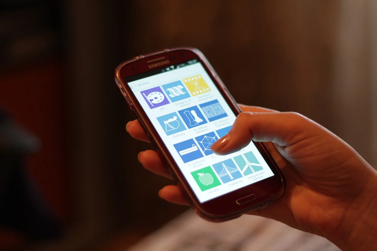 A hand holding a smartphone with app icons on screen, the kind of internet-connected device a hot wallet runs on