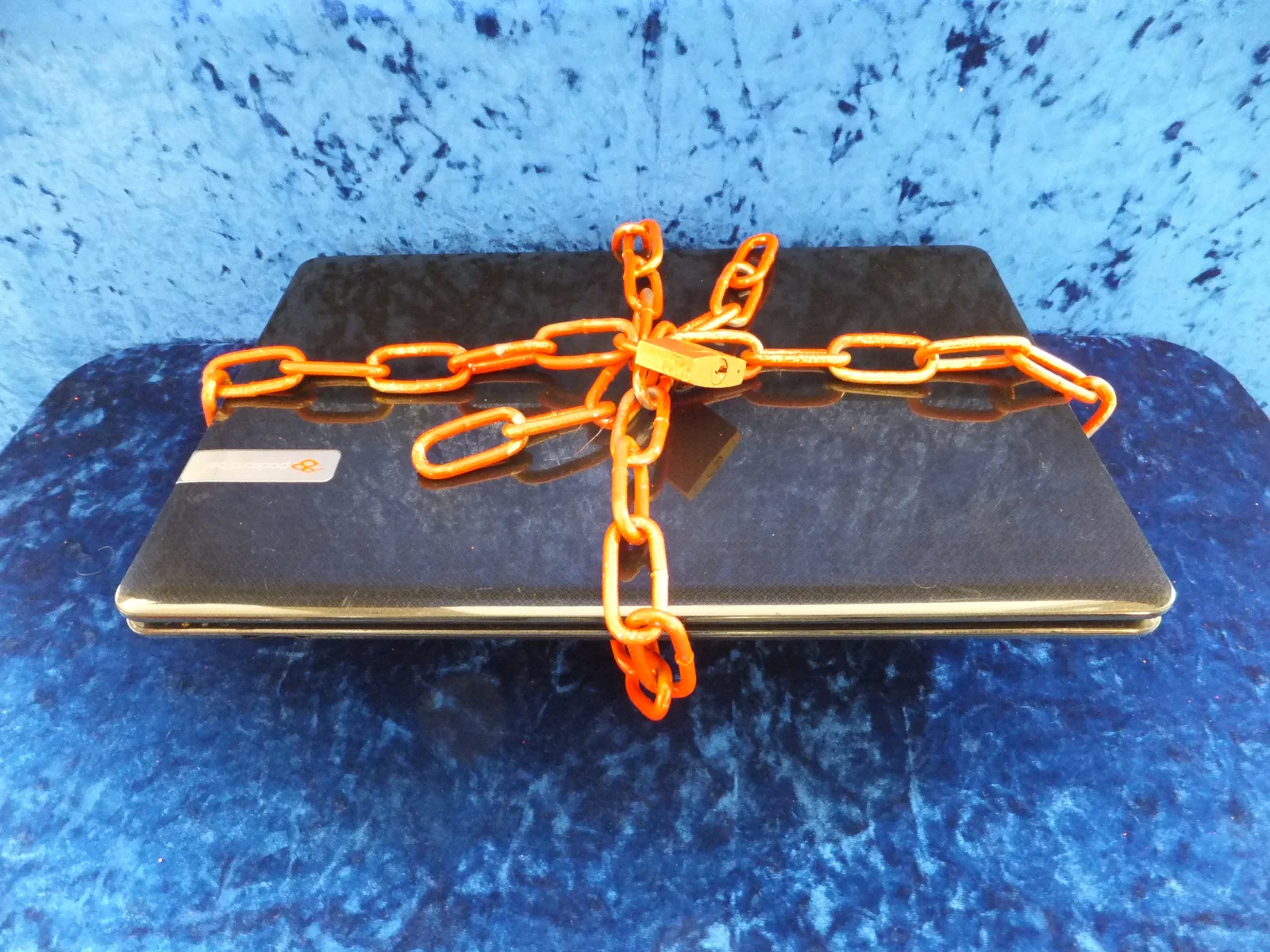 A closed laptop wrapped in a chain and padlock on a blue cloth, a reminder to lock down token approvals after you revoke them