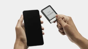 A person holding a Ledger Flex hardware wallet in one hand and a smartphone in the other during setup