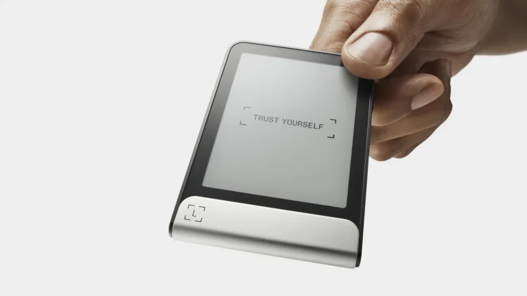 A hand holding the Ledger Flex hardware wallet, its 2.8-inch E Ink touchscreen showing the words Trust Yourself