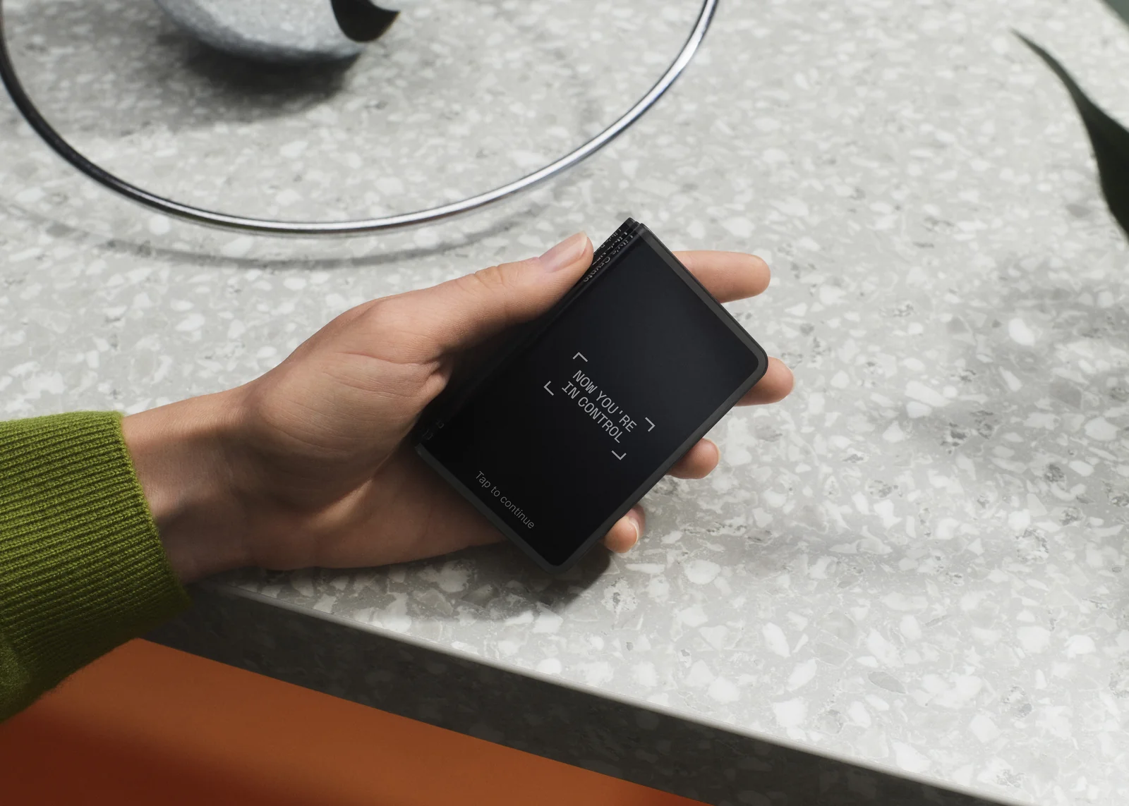 A hand holding a Ledger Stax on a stone countertop, showing the curved wrap-around screen