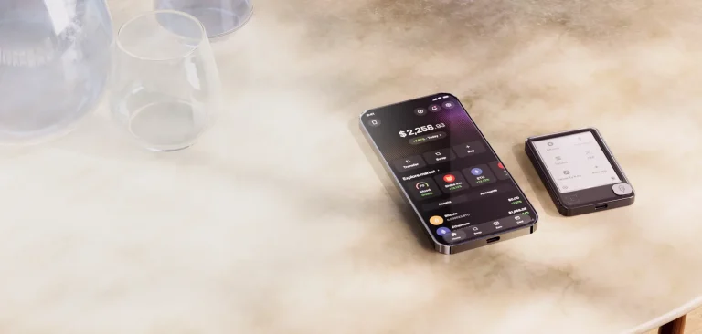 Ledger Wallet (formerly Ledger Live) app on a phone next to a Ledger Nano Gen5 signer on a marble table