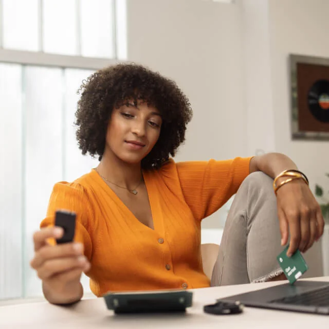 Person at a desk holding a Trezor Safe 3 hardware wallet in one hand and a backup card in the other