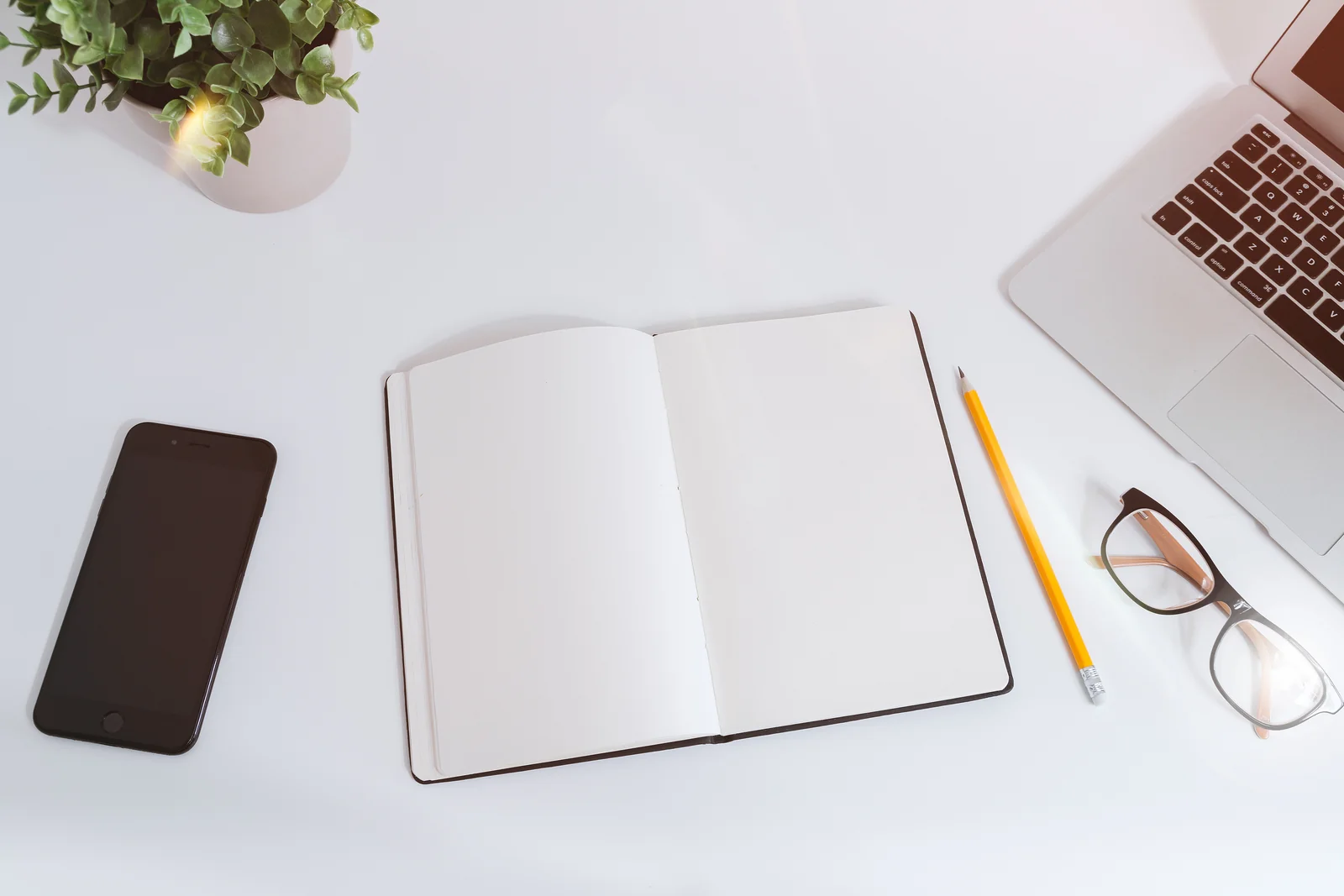 Smartphone, laptop and an open notebook on a white desk, the setup for comparing Phantom vs Backpack wallets