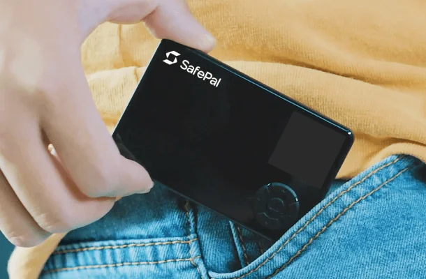 A hand sliding the card-sized SafePal S1 hardware wallet into a jeans pocket