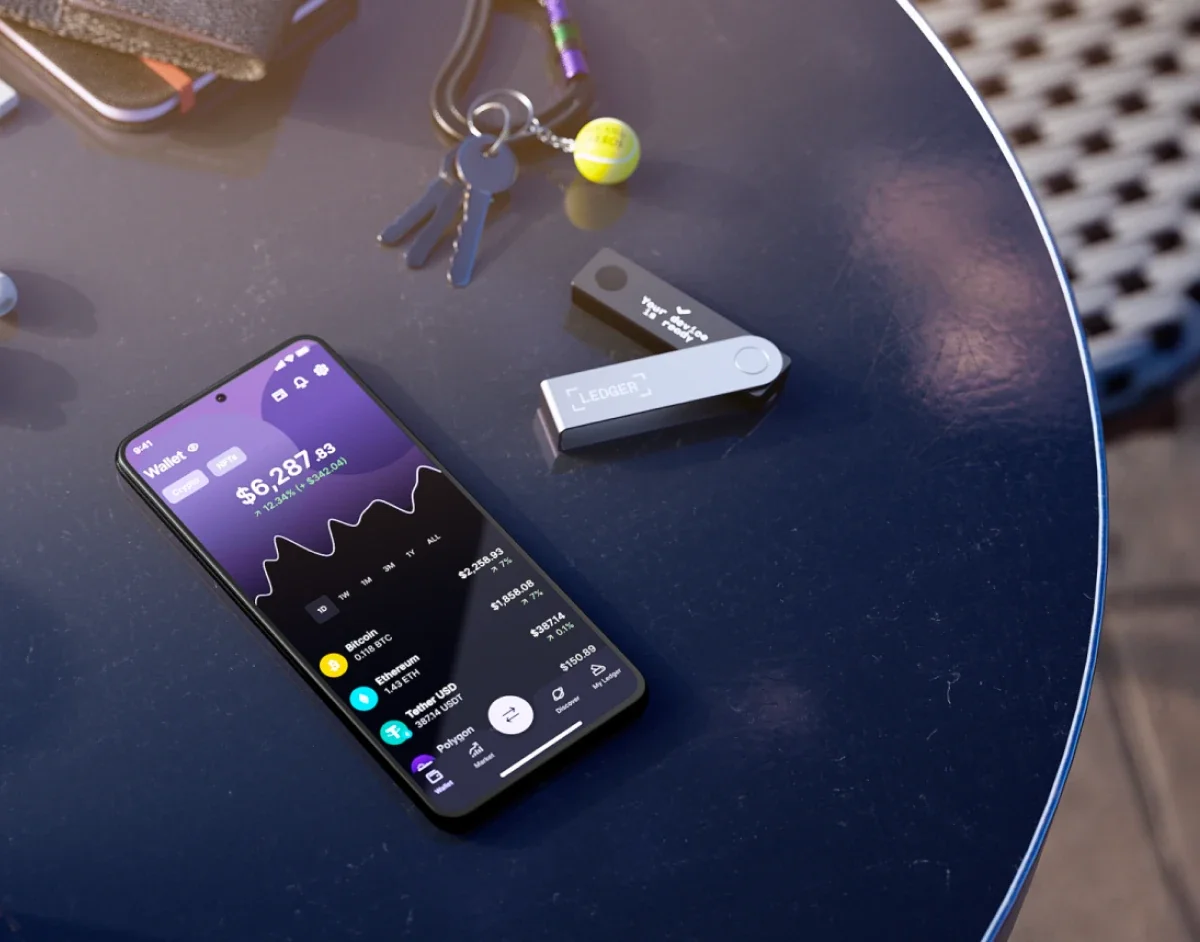 Ledger Nano X lying on a table next to a phone running the Ledger Wallet app