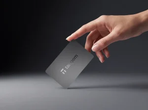 A hand holding a gray Tangem Wallet card by its corner above a light gray surface