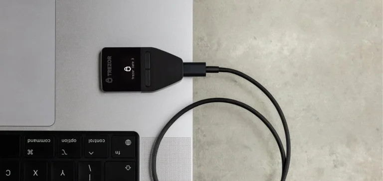 Trezor Safe 3 hardware wallet plugged into a laptop with its USB-C cable