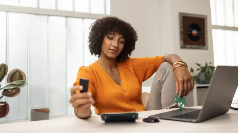 Person holding a Trezor Safe 3 hardware wallet at a desk with a laptop and a wallet backup card