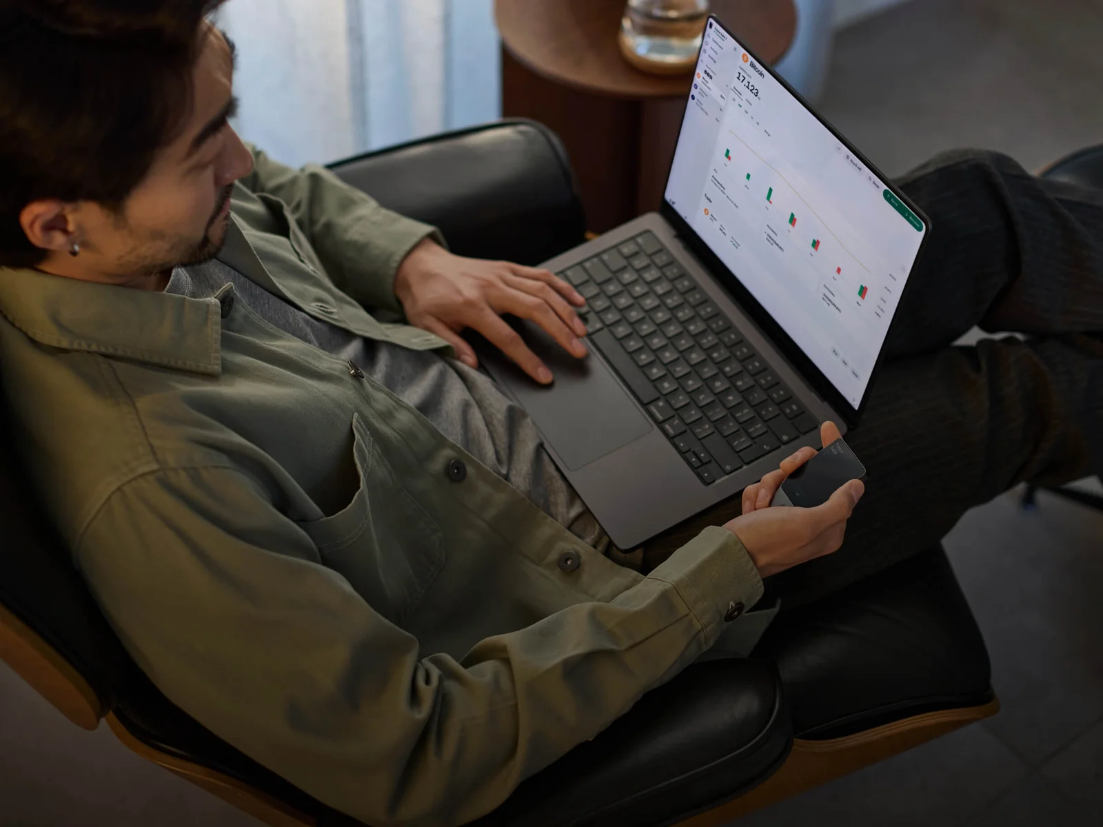 A person holding a Trezor Safe 7 hardware wallet next to a laptop running the Trezor Suite app