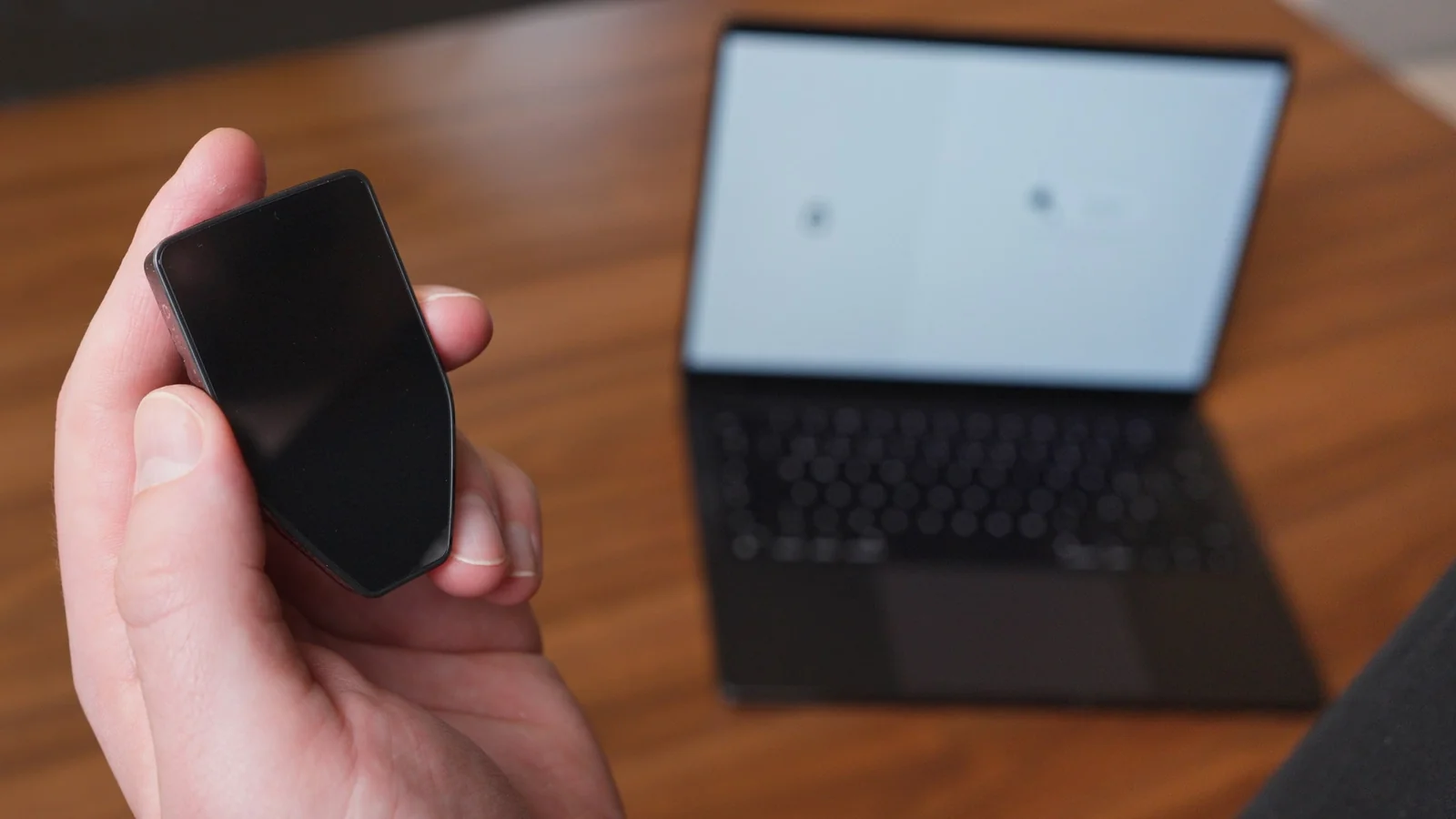 Hand holding a Trezor hardware wallet in front of a laptop used for Trezor Suite setup