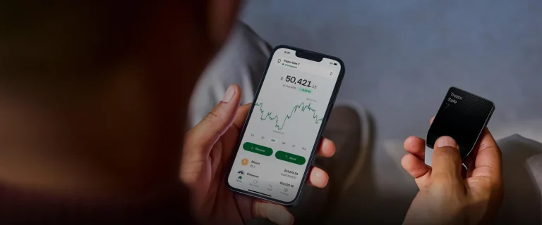 Trezor Suite mobile app showing a portfolio balance and chart on a phone, next to a Trezor Safe 7 hardware wallet