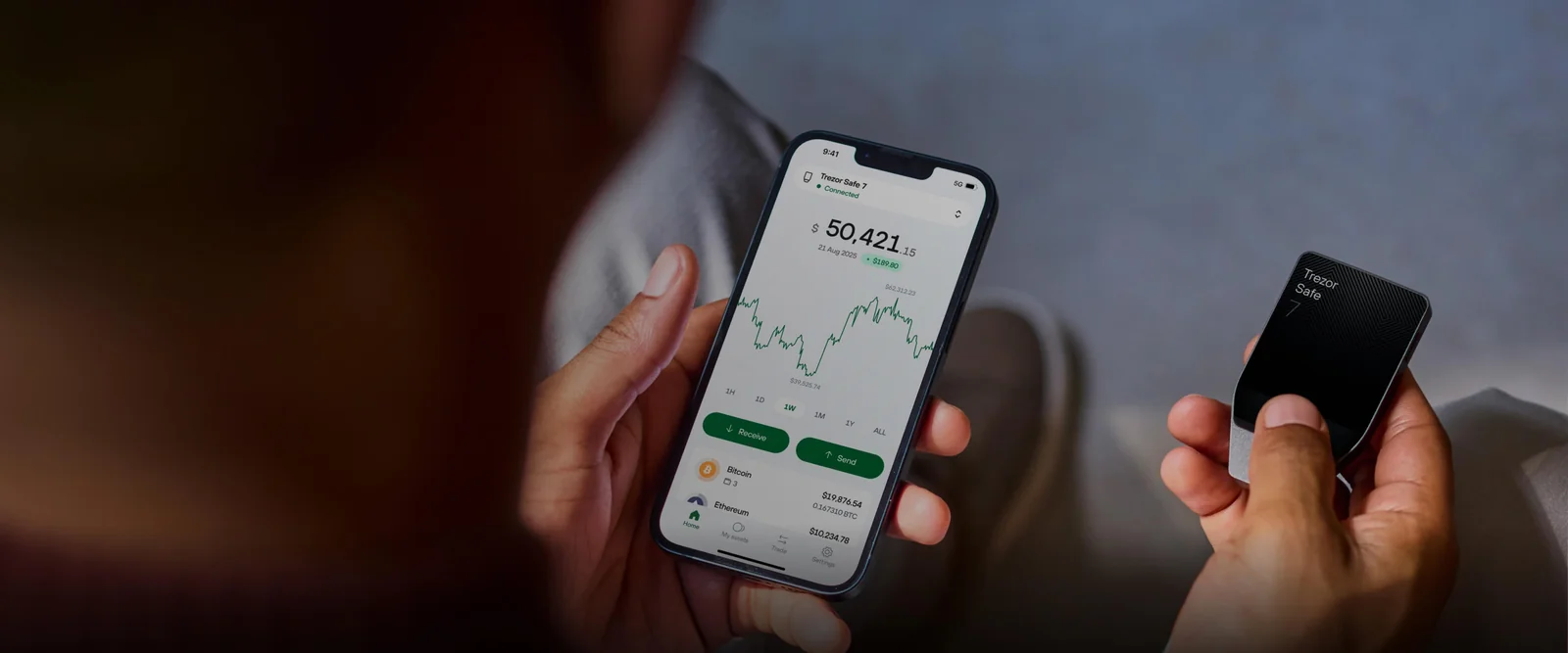 Trezor Suite mobile app showing a portfolio balance and chart on a phone, next to a Trezor Safe 7 hardware wallet