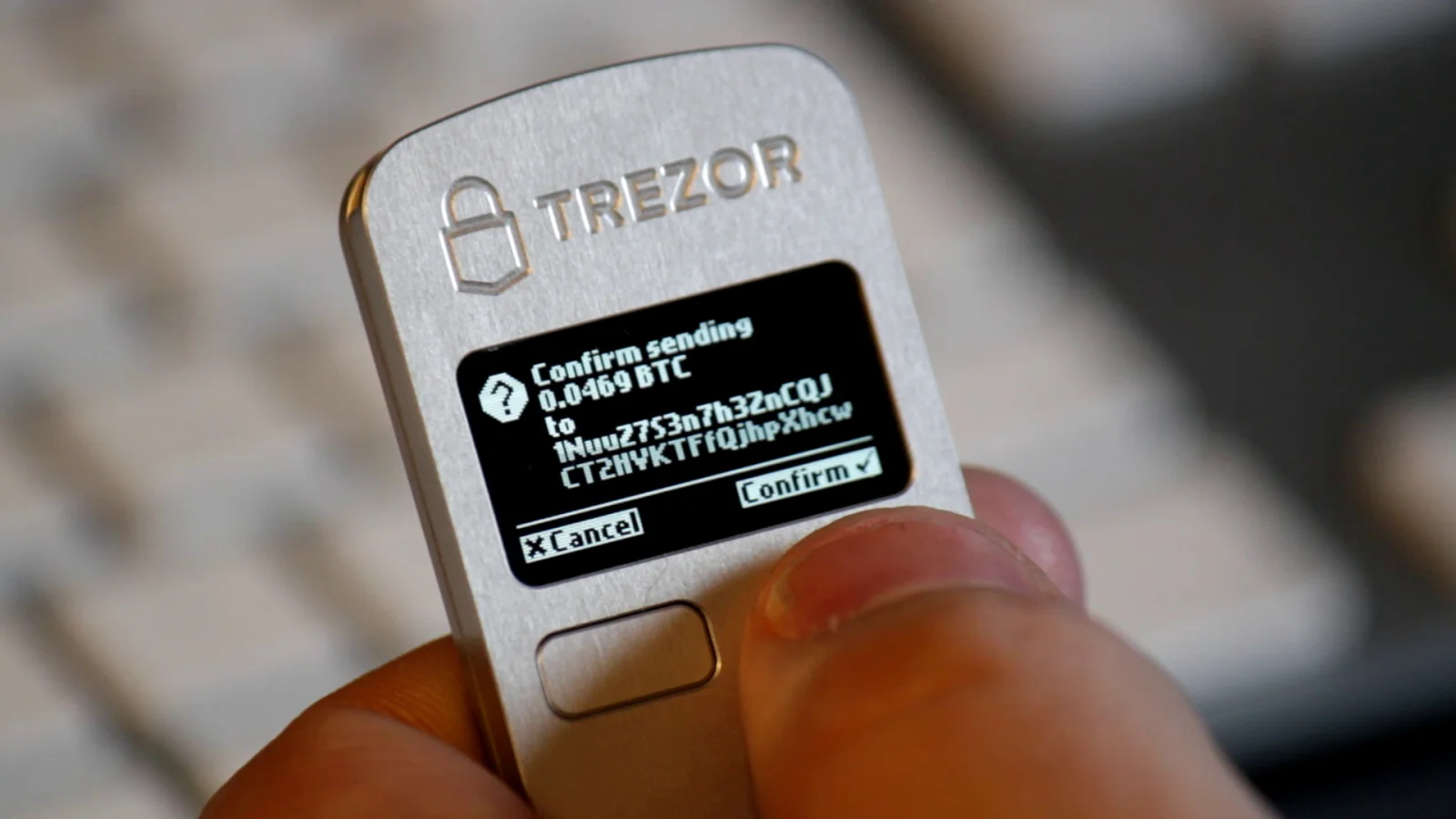 A Trezor hardware wallet held in a hand showing a confirmation screen, the screen that also displays the seed phrase during setup